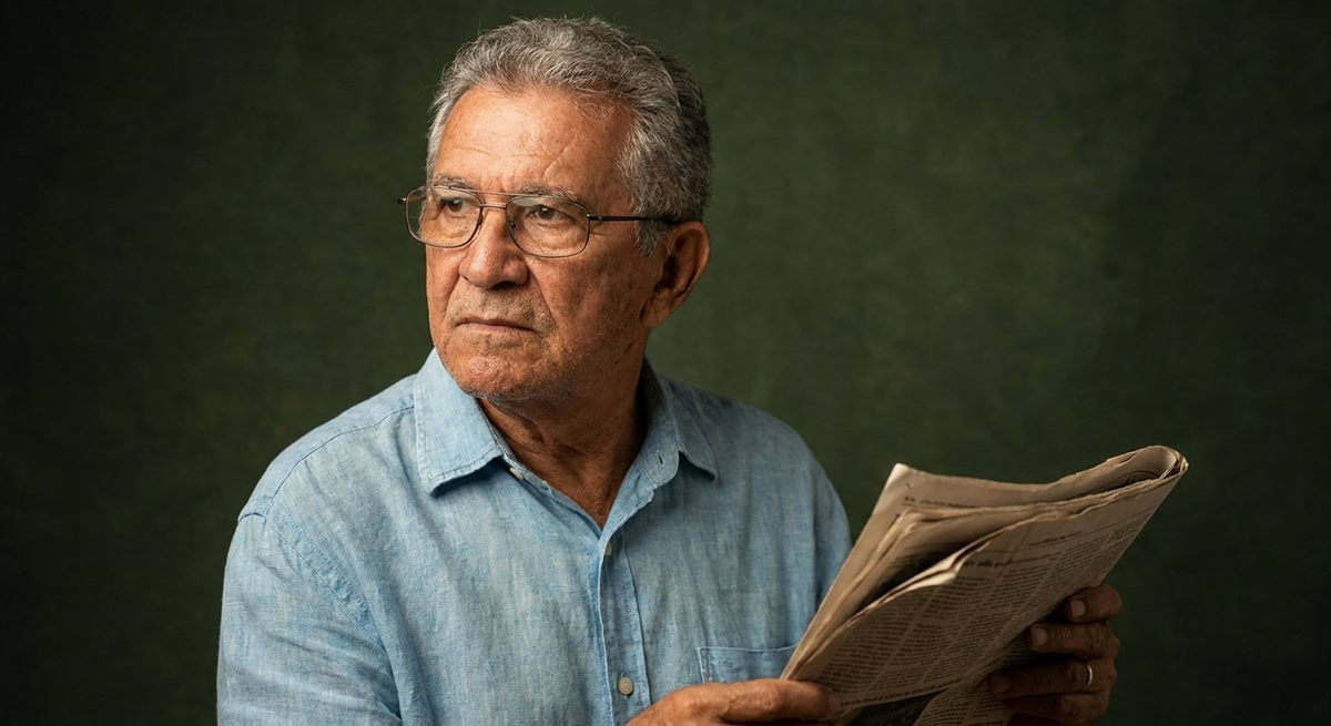 Homem mais velho de óculos segurando um jornal.